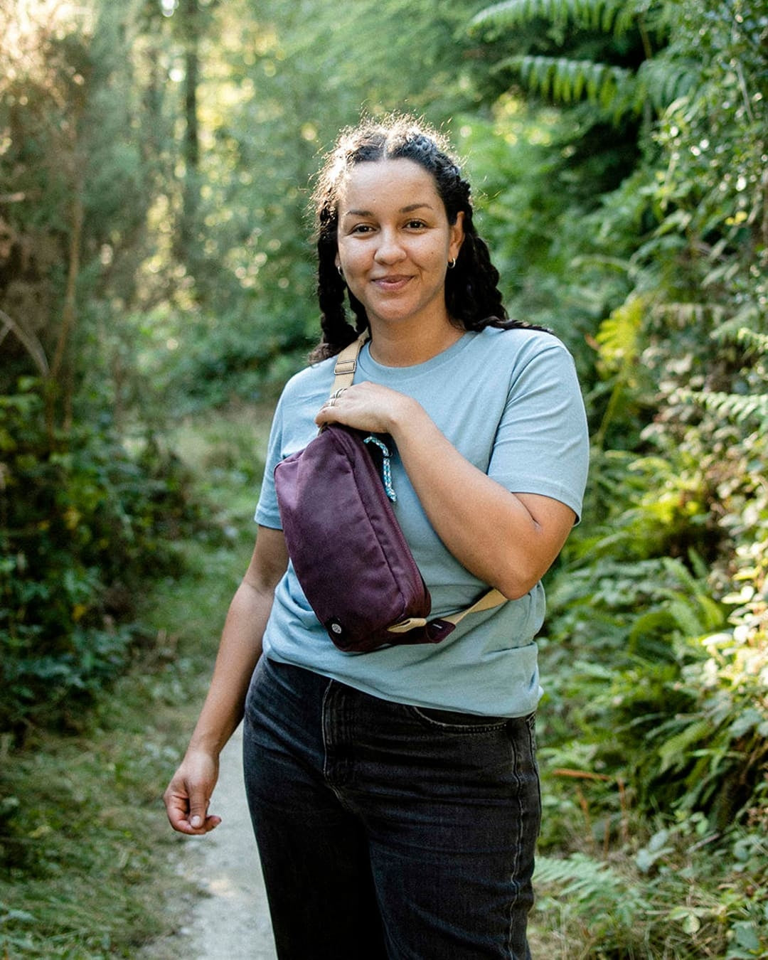 Smiling woman on a forest path wearing the Scout in cherry red waxed cotton across her chest