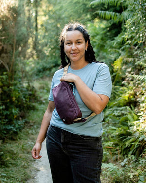 Smiling woman on a forest path wearing the Scout in cherry red waxed cotton across her chest