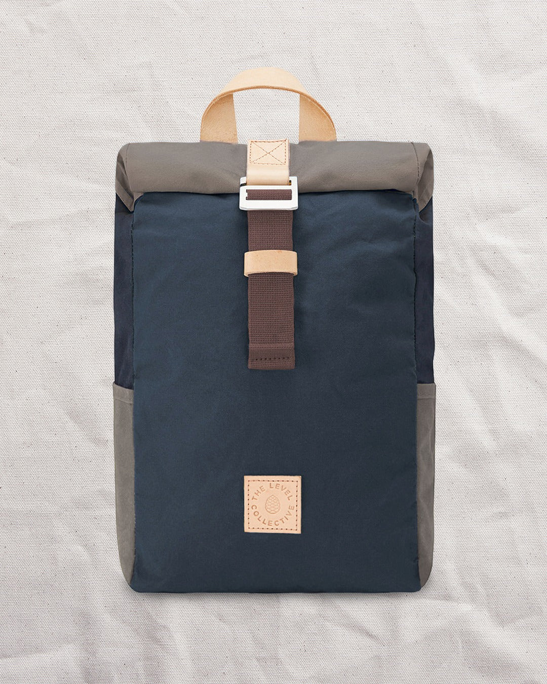 Front of the Navy & Stone roll top backpack: navy waxed canvas body, stone roll top and stone side pockets