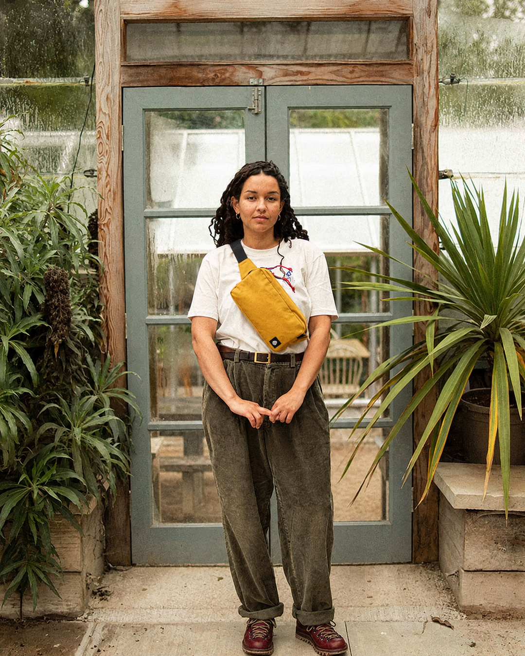 The Scout in Mustard worn cross body in front of a greenhouse door