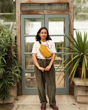 The Scout in Mustard worn cross body in front of a greenhouse door