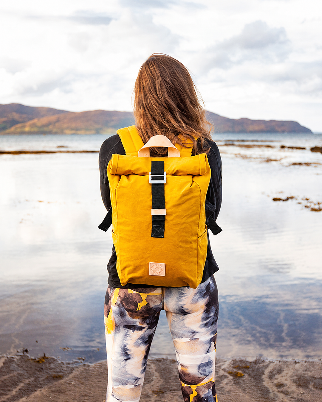 Mustard roll top canvas backpack worn on the shore of a Scottish loch, waxed cotton outdoor rucksack