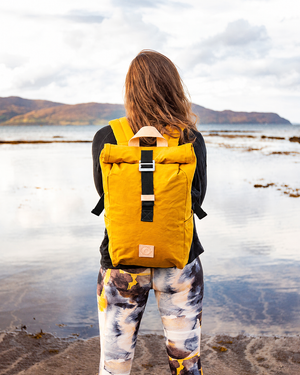 Mustard roll top canvas backpack worn on the shore of a Scottish loch, waxed cotton outdoor rucksack