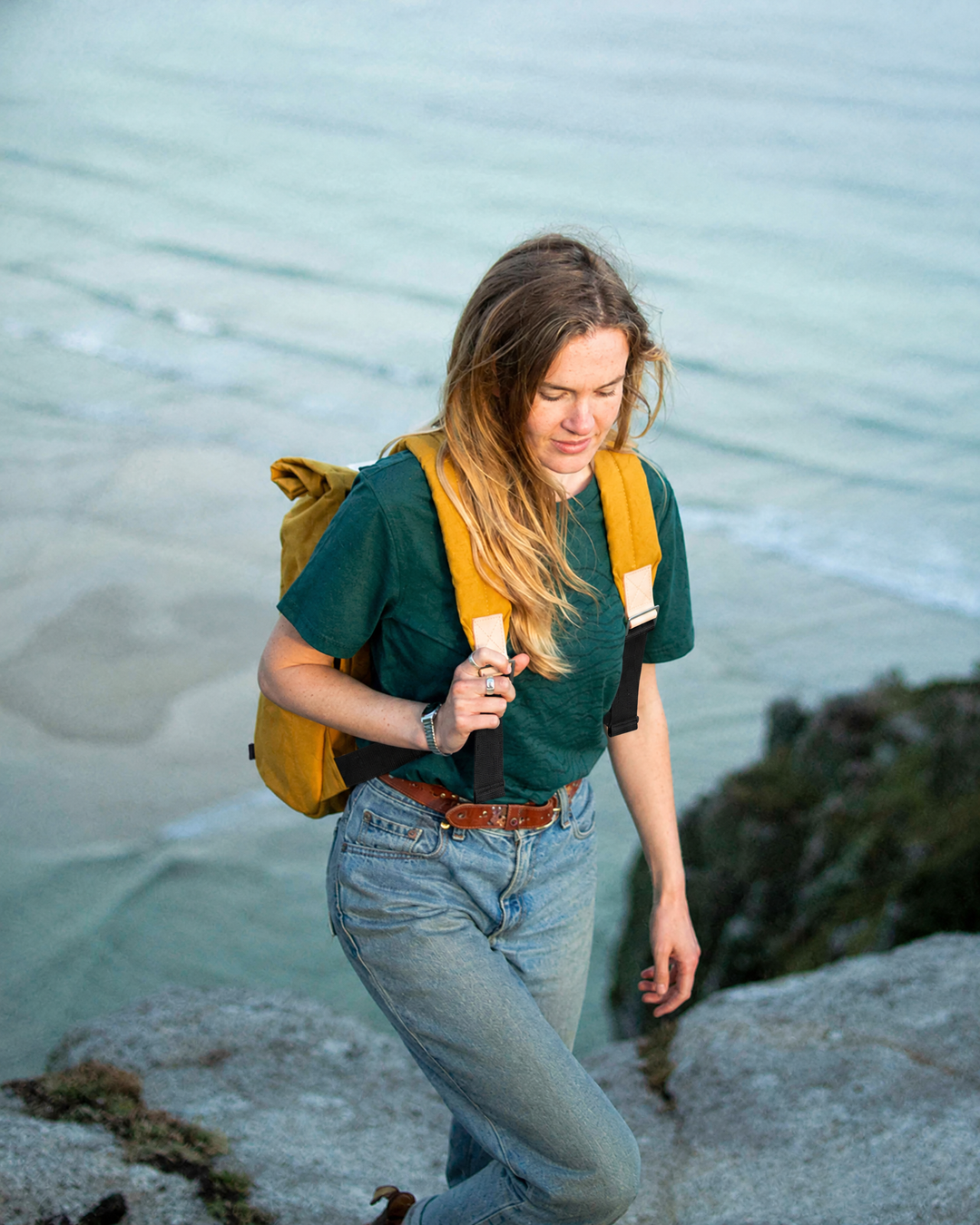 Woman walking on coastal rocks wearing the Mustard roll top backpack, British made waxed canvas backpack