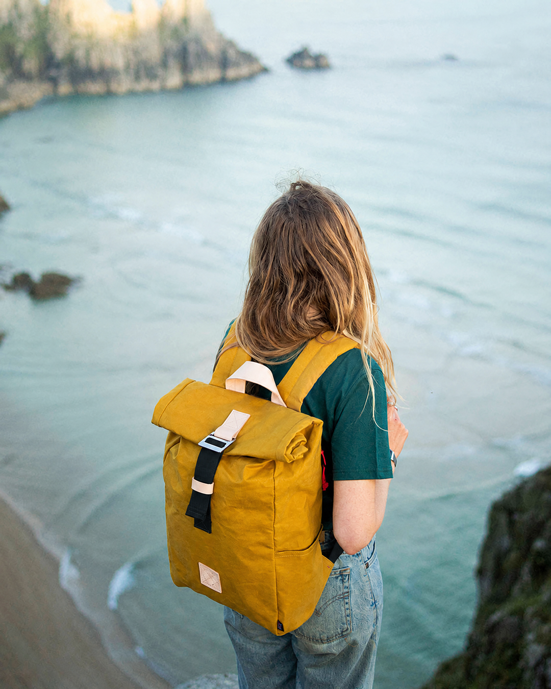 Winnats roll top backpack in Mustard waxed canvas on a Cornish clifftop above the sea, outdoor rucksack