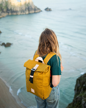 Winnats roll top backpack in Mustard waxed canvas on a Cornish clifftop above the sea, outdoor rucksack