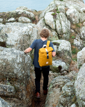 Mustard roll top backpack worn while scrambling between granite rocks, weatherproof outdoor backpack