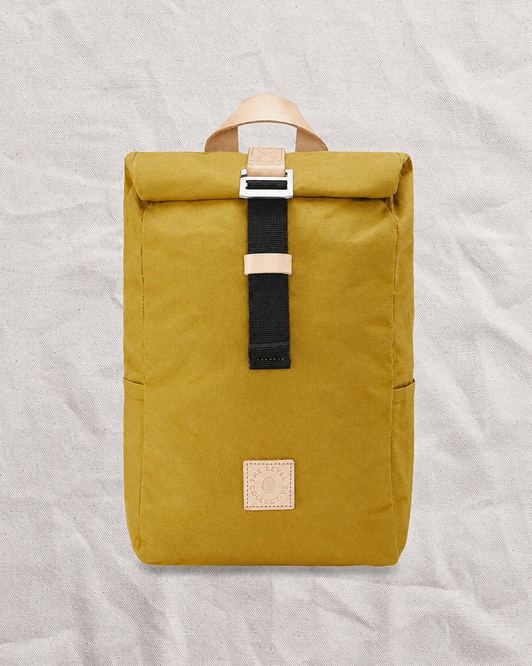 Winnats roll top bag in Mustard waxed organic cotton, front view with leather handle and patch