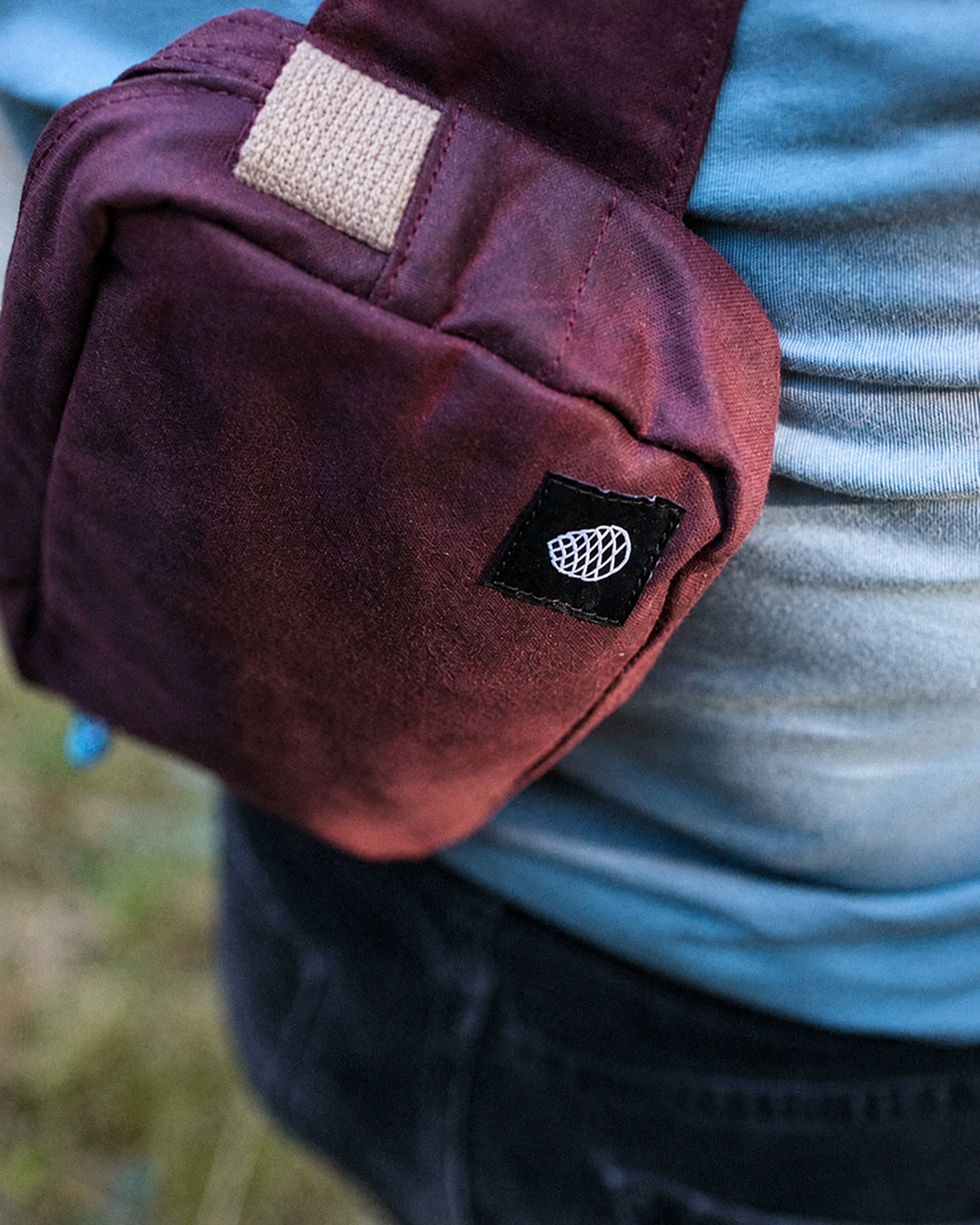 Close up of the Scout in cherry red waxed cotton with beige cotton webbing and woven pine cone label