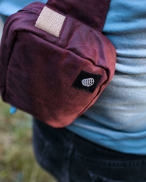 Close up of the Scout in cherry red waxed cotton with beige cotton webbing and woven pine cone label