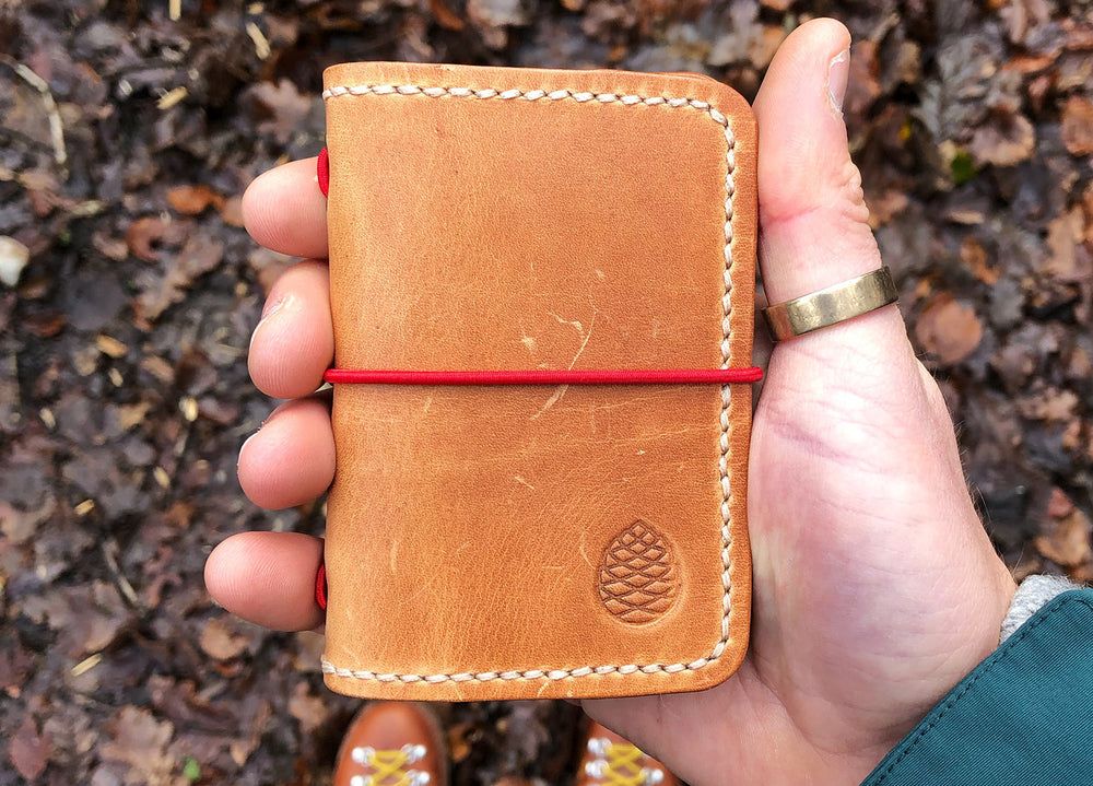 Leather Card holder wallet, hand stitched in small batches in Sheffield, UK. Pine Cone Logo imprinted on bottom right corner and a red elastic rope closure.