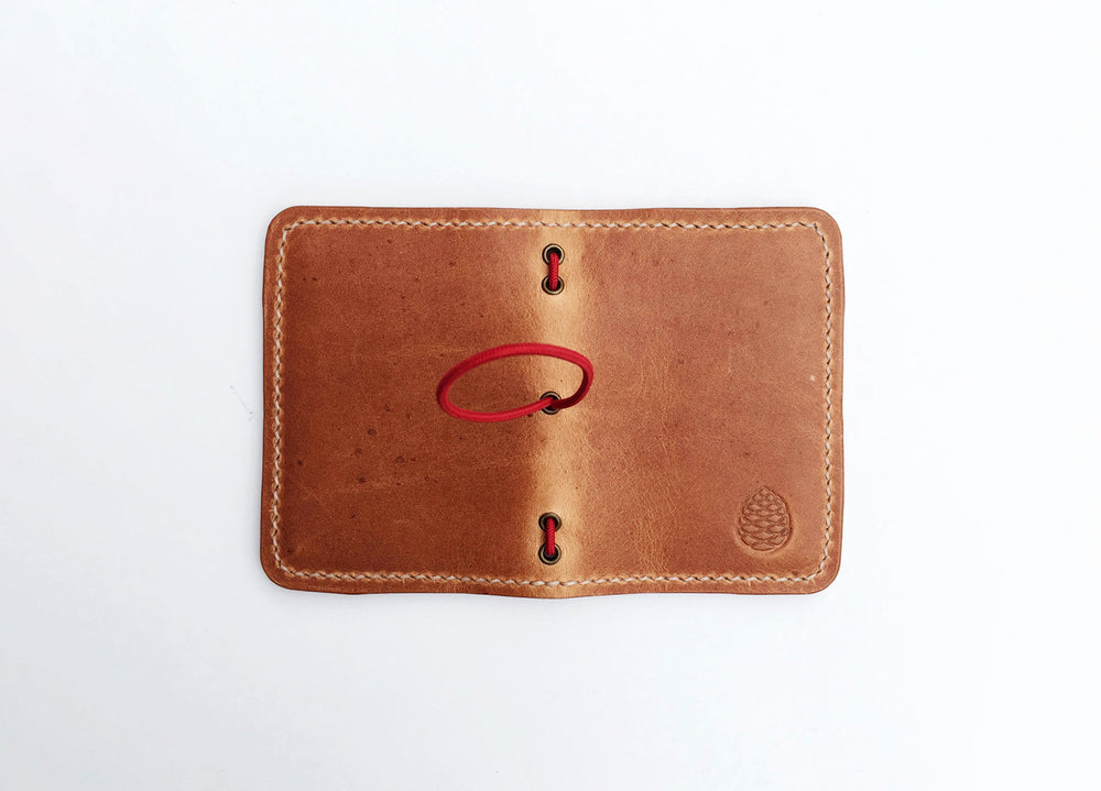 Leather Card holder wallet, hand stitched in small batches in Sheffield, UK. Pine Cone Logo imprinted on bottom right corner and a red elastic rope closure.