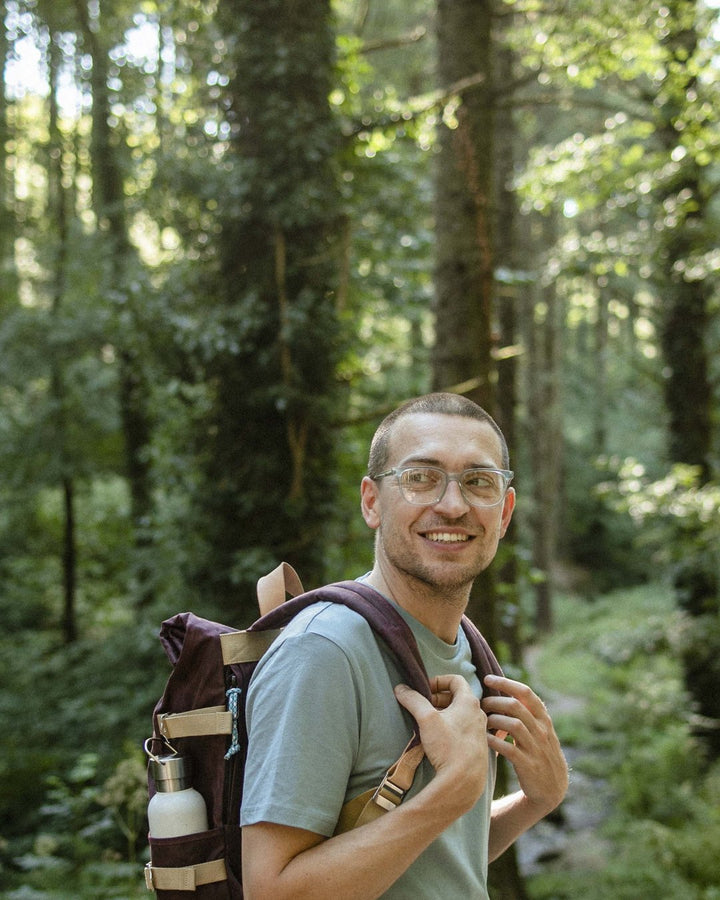 Smiling walker in the forest carrying a Winnats Roll Top in Cherry